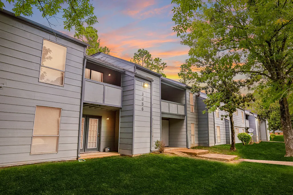 Two story apartment building with light grey siding and trees surrounding at dusk