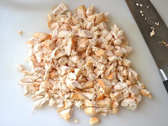 cooked chicken being chopped into small pieces with knife 