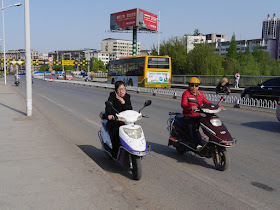 woman holding a mobile phone to her right ear with her left hand while driving a motorbike