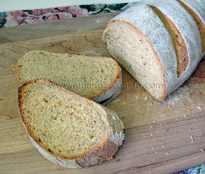 A photo of a sliced loaf of rustic rosemary garlic bread resting on a wooden cutting board.