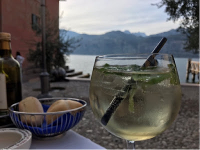 Vinglass med blankt innhold med sitronmelisse, isbiter og sugerør. Innsjø og fjell i bakgrunnen.