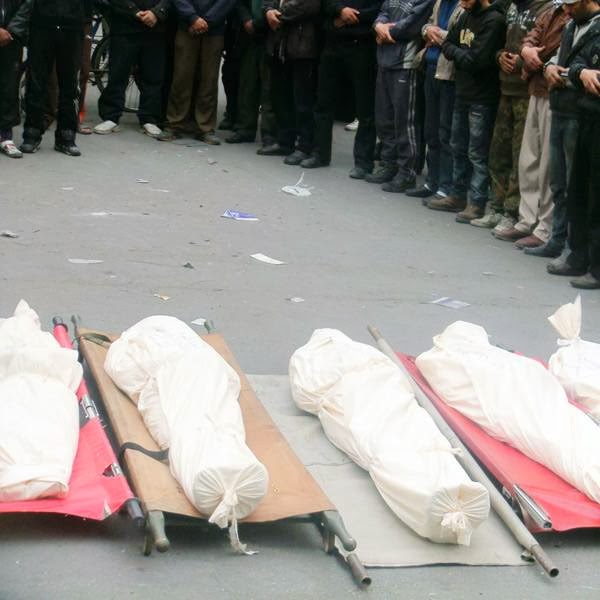 Residents of the Yarmuk Palestinian refugee camp mourn over dead bodies during a group funeral on January 26, 2014, south of the Syrian capital Damascus. Six people reportedly died as a result of food and medical shortages, while another was shot by a sniper as he was trying to collect grass to eat.