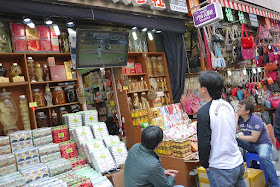 three men watching a American baseball game on a TV outside at a market