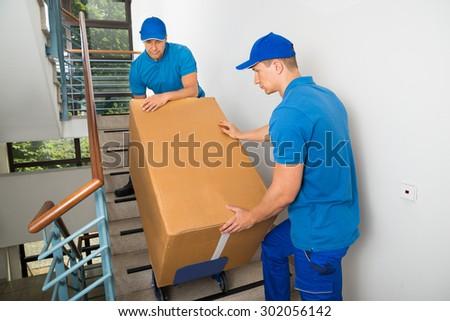 Two male movers carrying a box down the stairs