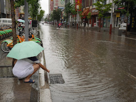 young man clearing debris from a grating for drainage on a flooded street in Taiyuan, China