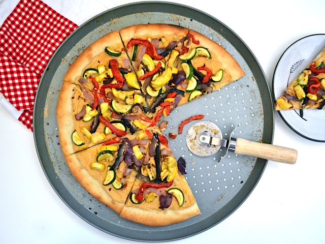 hummus grilled vegetable pizza cut with pizza cutter and two slices taken out 