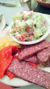 Bosanski Sudzuk (a Bosnian Smoked Beef sausage with light garlic and other light spicing) sliced and decoratively arranged with pickled vegetables and Sopska (a tomato and cucumber salad with diced tomato, cucumber, green pepper, and cheese in light sour cream dressing) served cold at Drina Daisy, a Bosnian Restaurant in Astoria, OR