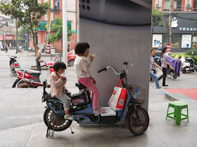 two girl eating while sitting on a parked electric bike in Changsha