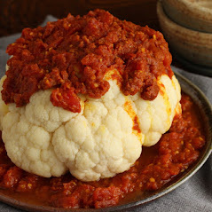 whole roasted cauliflower nestled on plate of spice tomato sauce