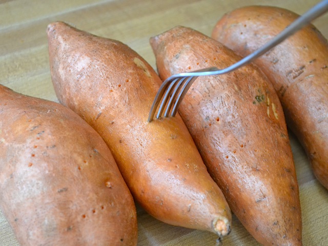 Four raw sweet potatoes being pricked with fork 