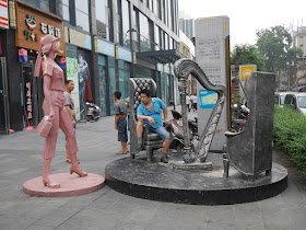 statue of stringless harp with two chairs, one of which is occupied by a real man sitting informally