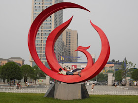 two boys lying on a large circular red sculpture