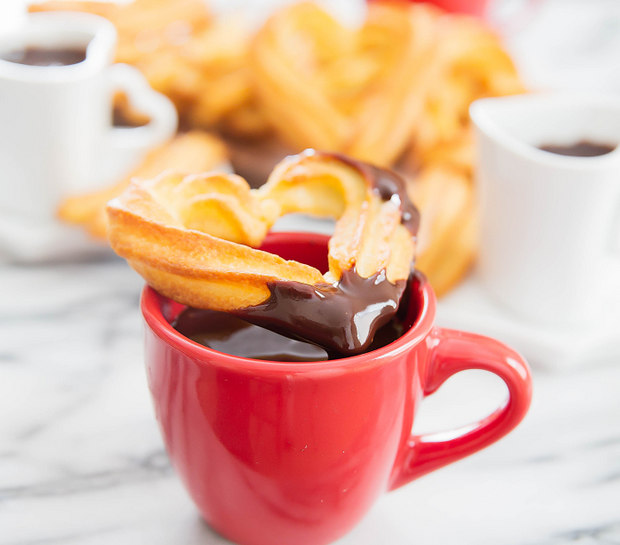 photo of a heart-shaped baked churro sitting on a mug of melted chocolate