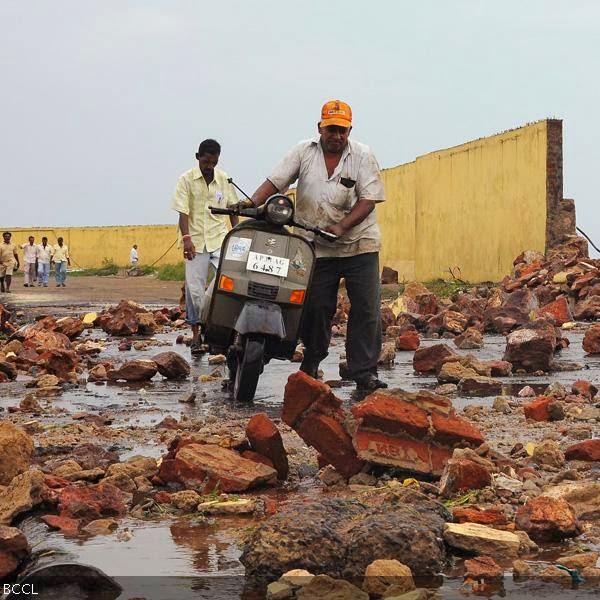 People walk among debris from a broken wall after it was damaged by a wave brought by Cyclone Phailin at a fishing harbour in Visakhapatnam district in the southern Indian state of Andhra Pradesh October 12, 2013. 