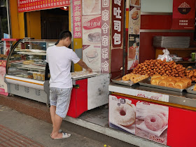 man playing a game of xiangqi alone next to a donuts & bread stand