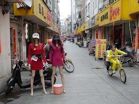 two girls on a bicycle passing mannequins in Yangjiang, China