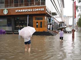 people crossing a flooded street next to a Starbucks in Taiyuan, China