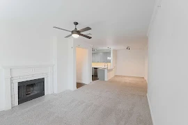 Open concept living, kitchen, and dining areas with light tan carpet, white walls, ceiling fan, and tiled fireplace