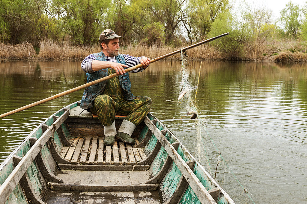 An elderly angler on a river inspects his wooden gear
