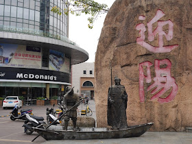 statues of two men on a boat in front of large Chinese characters and a McDonald's