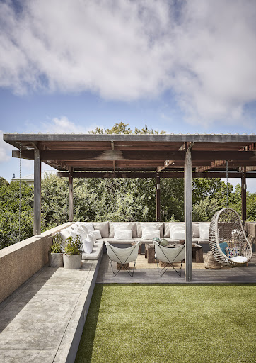 Various seating options underneath a sleek slatted pergola overlooking lush surrounds.