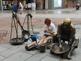 woman checks here mobile phone while sitting on a sculpture's small stool