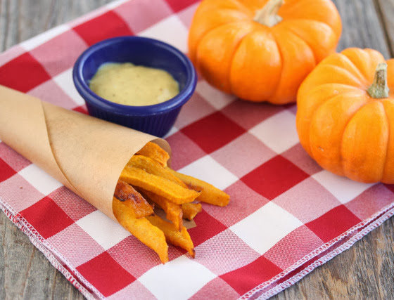 pumpkin fries in a paper cone on a red checkered napkin with dipping sauce on the side