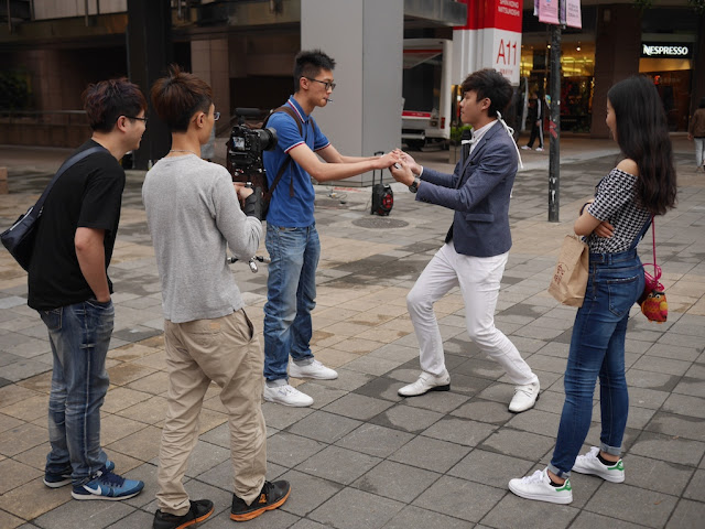 magician doing a magic trick for a young man while his girlfriend watches and person video records