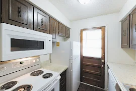 Kitchen with white appliances, speckled countertops, wooden cabinets, wood-inspired flooring, and exterior door with window