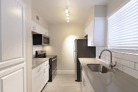 Kitchen with tile backsplash, stainless steel appliances, light-wood inspired flooring, white cabinets, and grey countertops