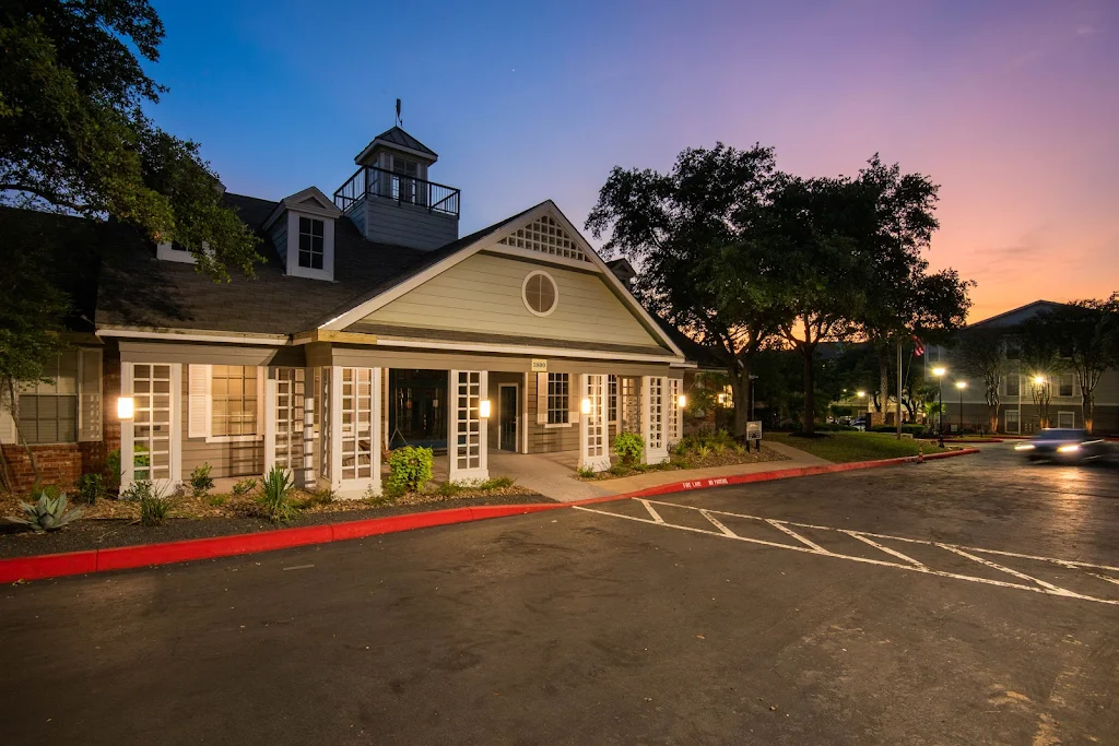 Twilight view of an apartment complex clubhouse with illuminated windows and a parking area