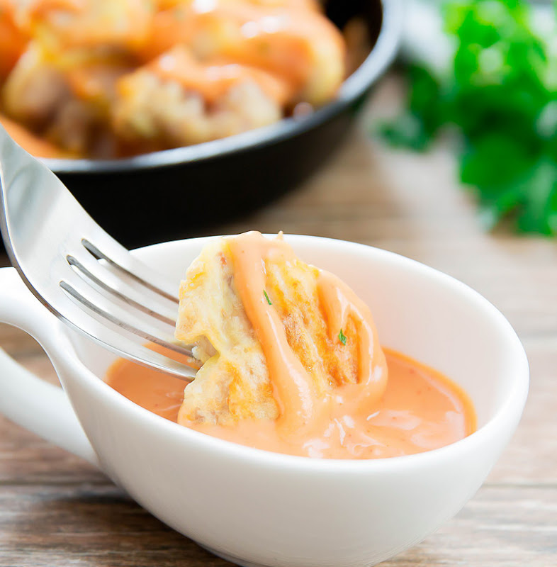 close-up photo of a piece of chicken being dipped in bang bang sauce