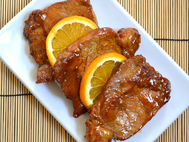 Top view of a plate of orange molasses pork chops with orange slices 