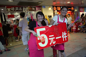 two young women hold a sale sign in front of a store at Dongmen in Shenzhen, China