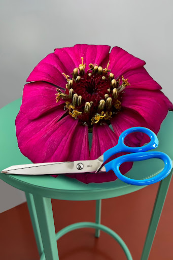 A large pink flower and blue industrial scissors are on top of a green stand.