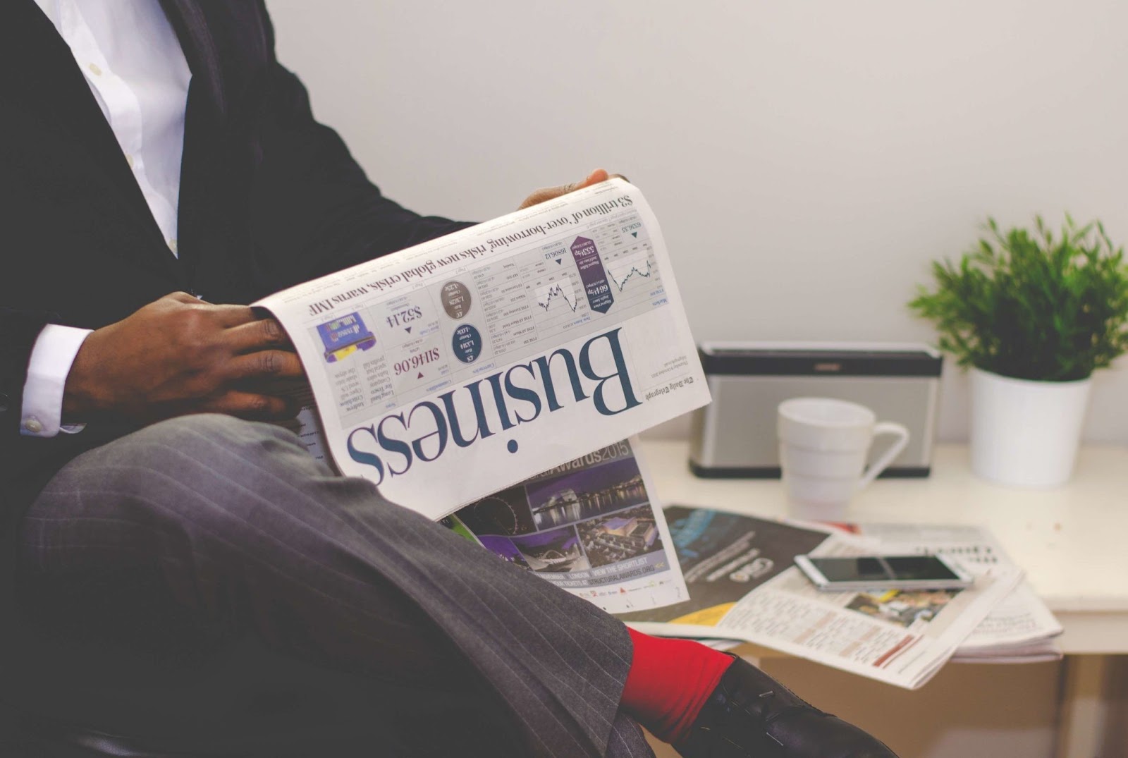 A seated man in a suit reading a newspaper
