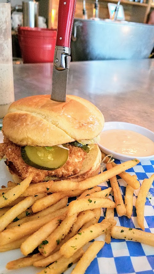 Shipwreck PDX food dish of Chicken Fried Fish Sandwich with tartar sauce, pickles, lettuce, potato bun, fast food fries, spicy dipping sauce