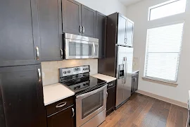 Kitchen with wood-inspired flooring, a window with blinds, dark cabinets, stone backsplash, and stainless steel appliances  