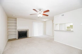 Living area with carpet, light walls, built-in shelving to the left of a fireplace with tile surround