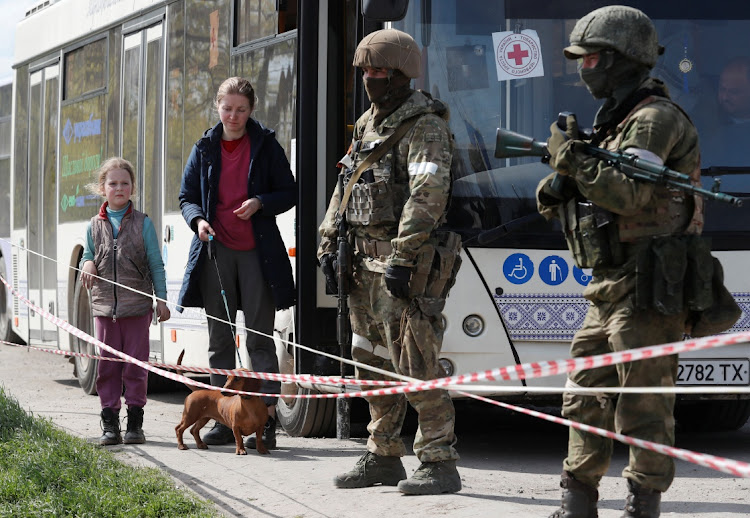 Civilians who left the area near Azovstal steel plant in Mariupol stand with a dog next to a bus guarded by service members of pro-Russian troops near a temporary accommodation centre during Ukraine-Russia conflict in the village of Bezimenne in the Donetsk Region on May 1 2022.