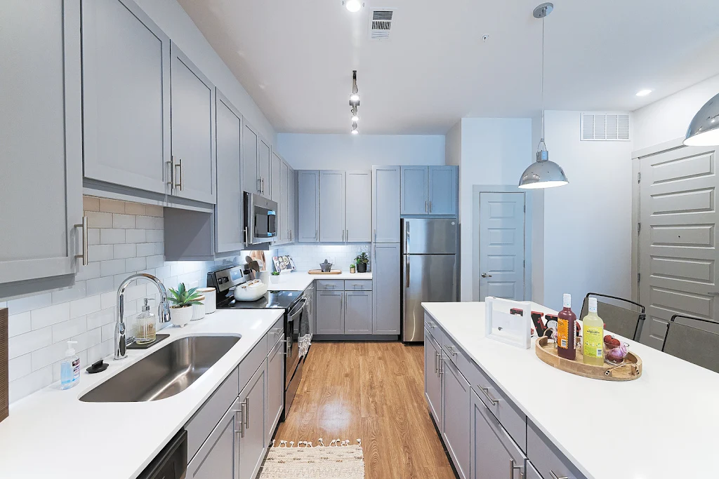 Furnished kitchen with wood flooring, gray cabinets, white tile backsplash, and white stone countertops