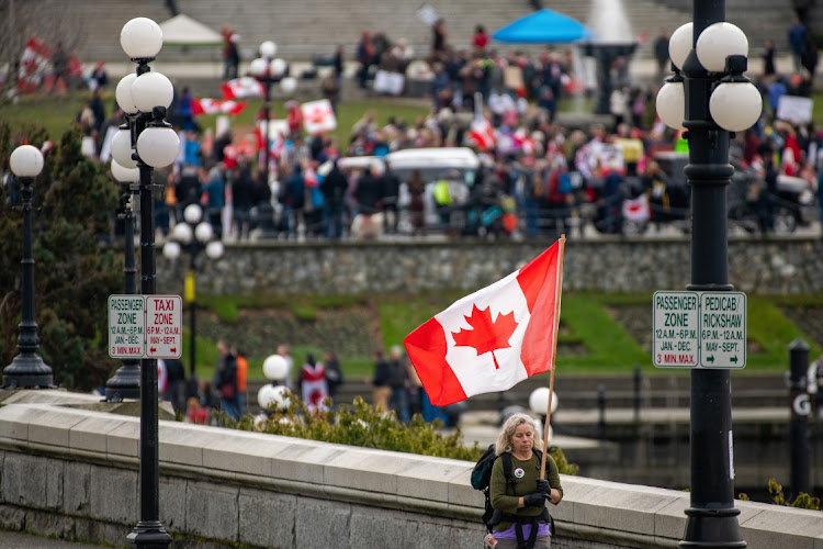 A protester walks with a Canadian flag near the Legislative Assembly of British Columbia during a demonstration in Victoria, British Columbia, Canada, on Saturday, Feb. 5, 2022. Tensions boiled over at protests against vaccine mandates in two Canadian cities as demonstrations that began with frustrated truckers spread across the nation and are threatening to spill into the U.S.