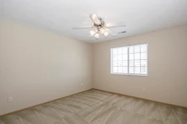 Bedroom, facing double window, with beige carpet and walls, oak trim, and a ceiling fan