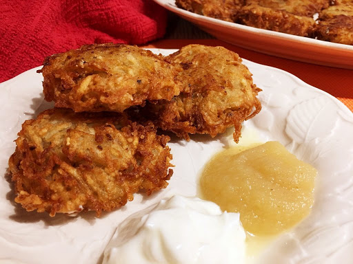 Three fried potato latkes on a plate with sour cream and apple sauce.