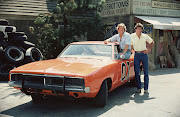 American actor Byron Cherry (as Coy Duke) sits in the window of the 'General Lee,' the famous orange Dodge Charger from the television series 'The Dukes of Hazzard,' August 1982. Christopher Mayer (as Vance Duke) stands next to him. Cherry and Mayer were hired for the 1982-1983 season to replace Tom Wopat and John Schneider who walked off the show due to contract disputes. Wopat and Schneider returned the next season.