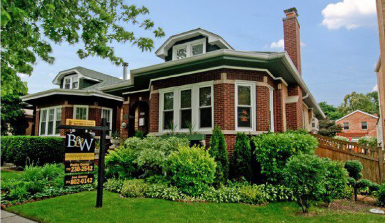 A lovely brick residential home in the Forest Glen neighborhood of Chicago, Illinois. There is a real estate sign posted in the front yard.