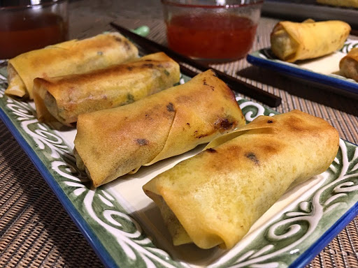 A few egg rolls sitting on a plate with some dipping sauces in the background.