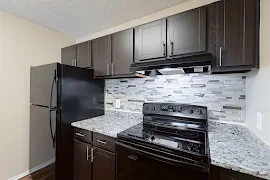 Modern kitchen in apartment with stainless steel appliances, dark cabinetry, and a tiled backsplash.