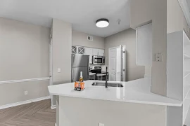 Modern apartment interior with stainless steel appliances, white countertops, and wood flooring.