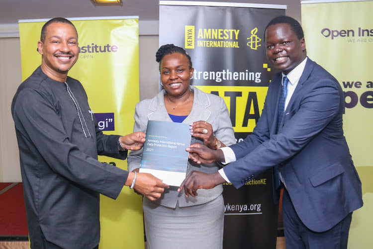 Amnesty International Kenya's executive director Irungu Houghton(L) and Policy officer Victor Ndede(R) hand over a copy of the report to the Commissioner office of the Data Protection Commission, Immaculate Kassait at Sarova Panafric Nairobi during the launch of the subnational data practices in Kenya study and comparative data reports that seek to ensure Kenya operationalizes the Data Protection Act.